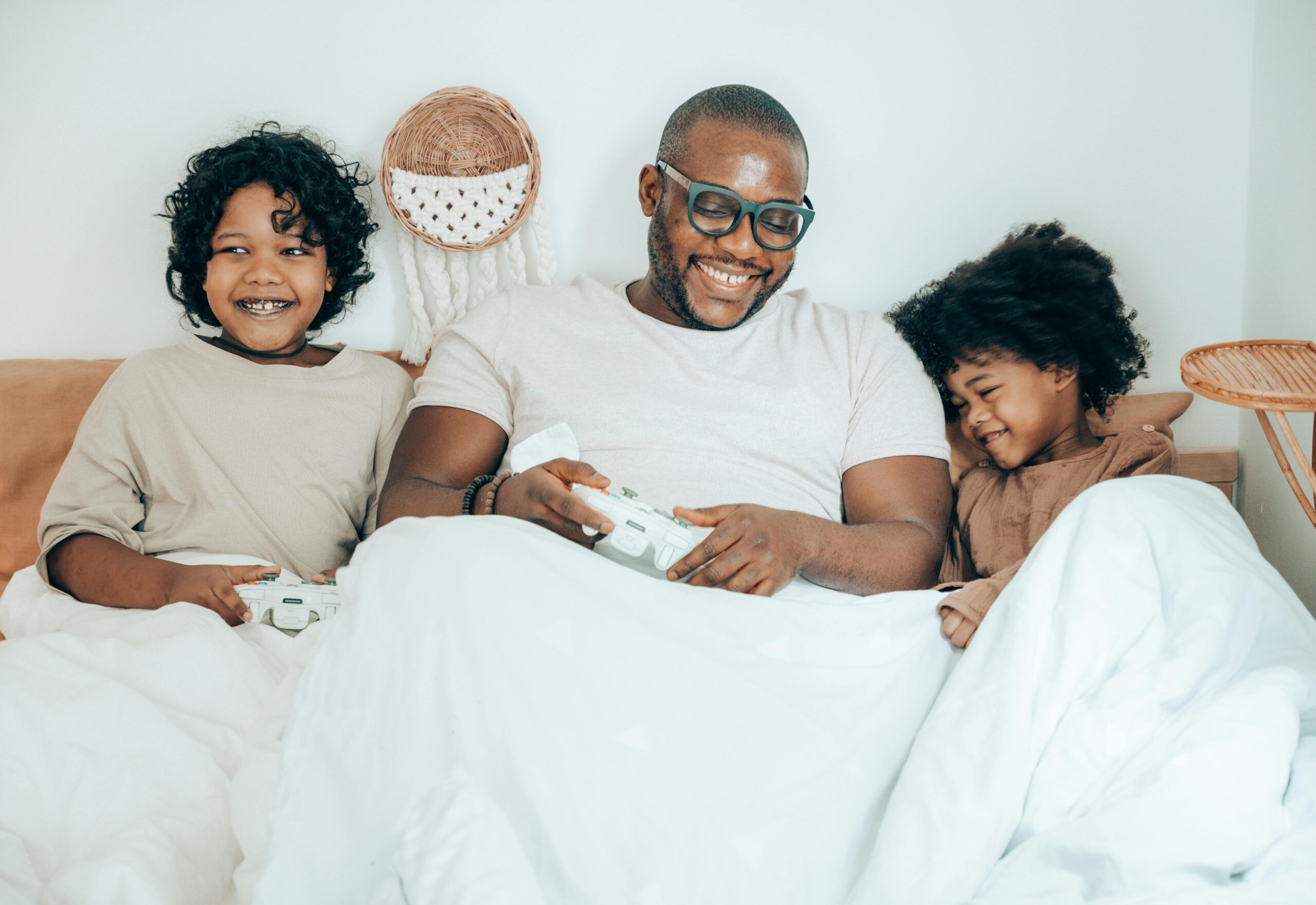 Children and dad in bed with game controllers in hand